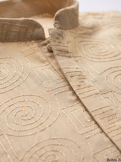 Close-up of a beige fabric garment with tonal geometric and spiral embroidery, showing the collar and front placket.