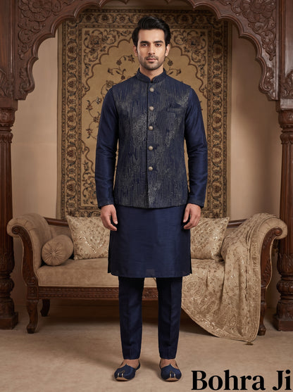 A man modeling a traditional Indian outfit consisting of a navy blue patterned waistcoat (kandha) and matching trousers (kurta and pajama set) in a richly decorated room with wooden arches and a patterned tapestry. The brand name 'Bohra Ji' is visible in the bottom right corner.