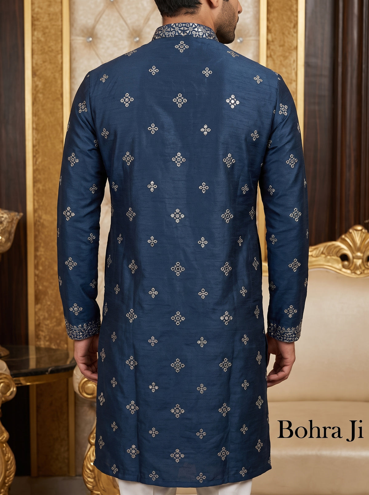A man viewed from the back wearing a navy blue long kurta with small metallic gold motifs and a patterned collar, standing in an ornate indoor setting with gold-trimmed furniture. The text 'Bohra Ji' appears in the lower right corner.