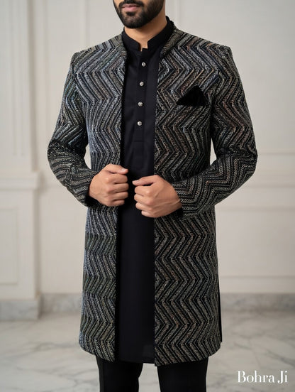 Man wearing a patterned coat over a black shirt against a neutral, open indo western jacket background. 