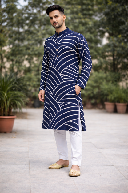 Man wearing a blue and white patterned kurta with white pants outdoors.